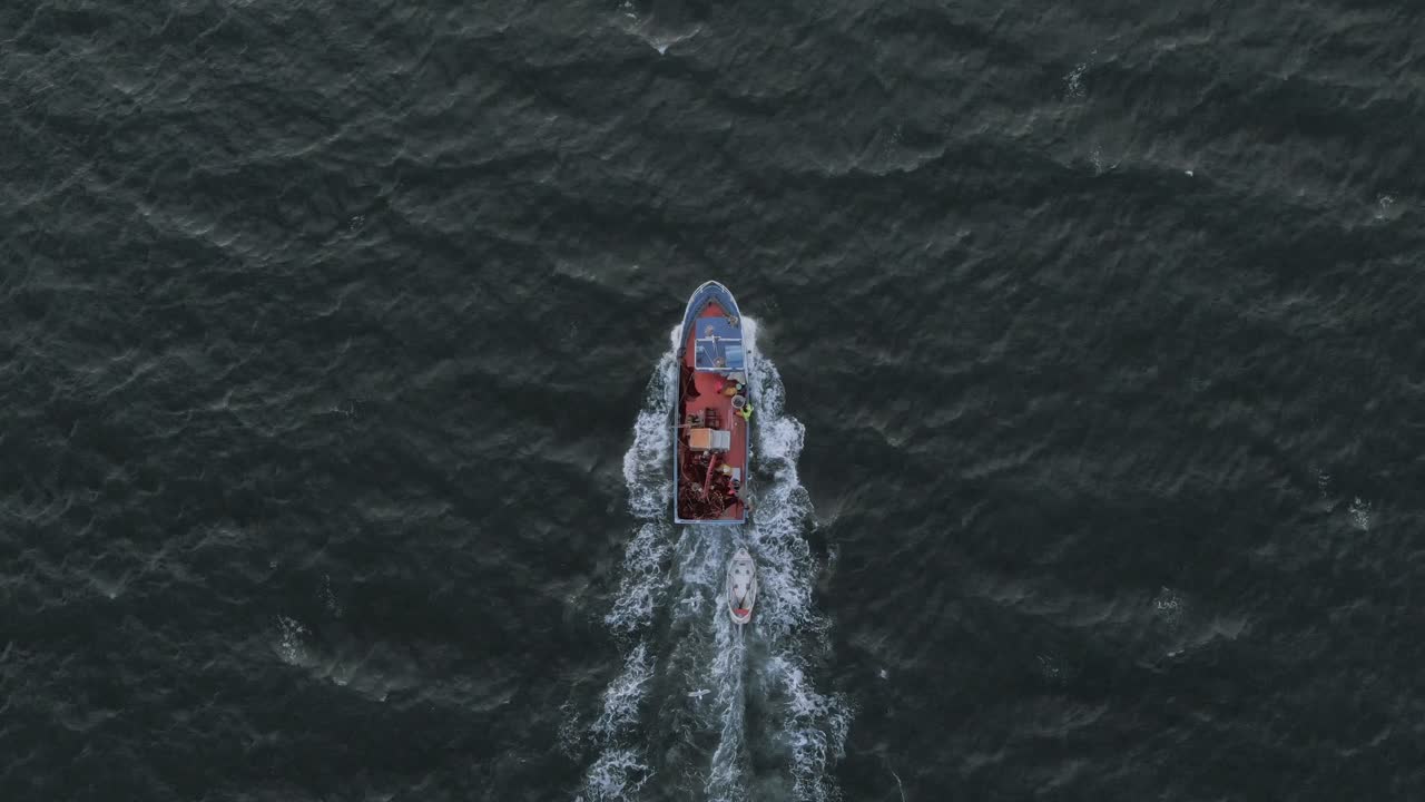 un barco de pesca en rápido movimiento cortando a través de las olas en el océano durante el amanecer desde un ángulo de vista de pájaro tomado de un avión no tripulado en el cielo