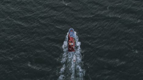 A-fast-moving-fishing-boat-chopping-through-the-waves-in-the-ocean-during-sunrise-from-a-birds-eye-view-angle-taken-from-a-drone-in-the-sky