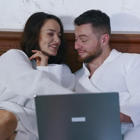 beautiful couple in love sitting on bed and watching movie on laptop. happy holidays of a young man and woman. vacation and honeymoon concept