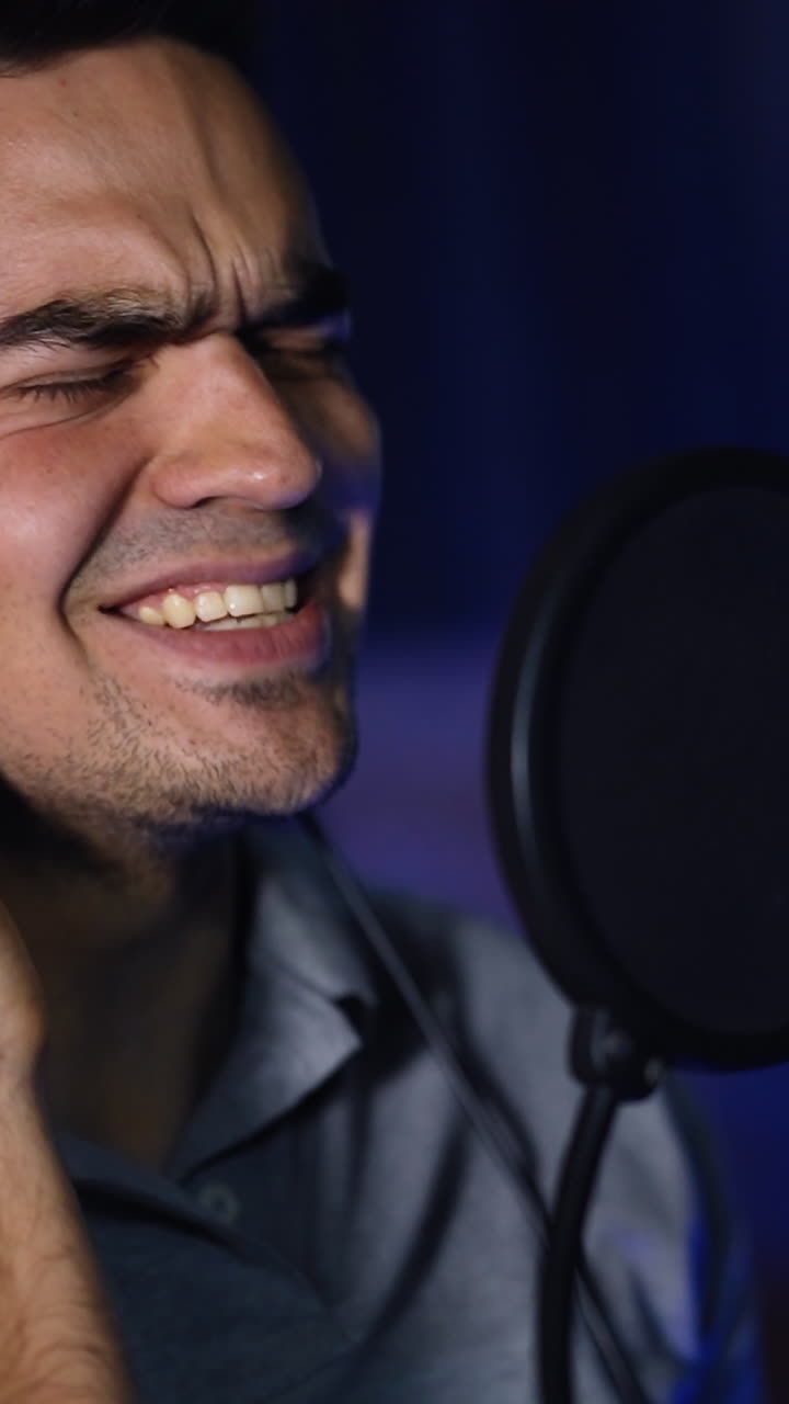 Man closing eyes during emotional song performance in the studio. Close up portrait at blurred background of dark studio. Vertical video