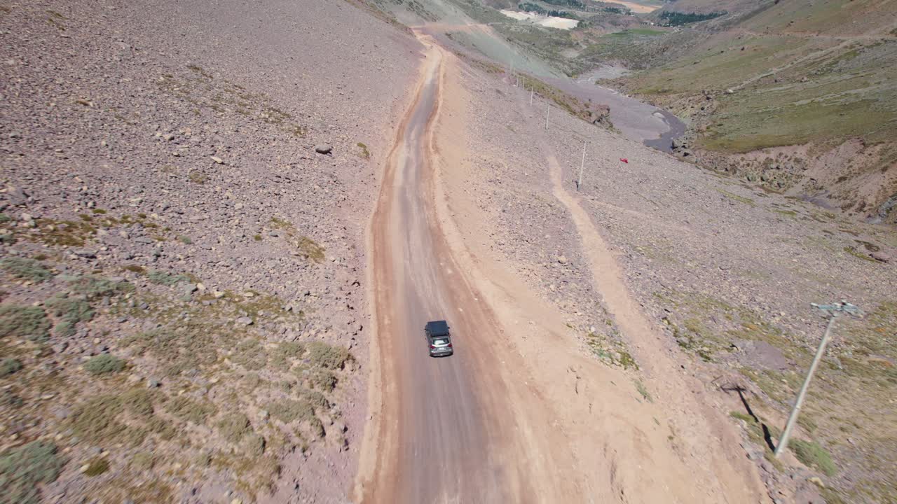 coche solitario conduciendo por una carretera sin pavimentar dentro de la cordillera de los andes en un día soleado de verano en chile