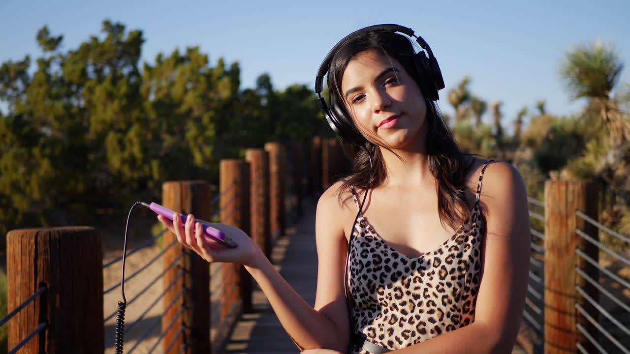 una hermosa joven que se ve feliz escuchando música desde un teléfono inteligente en sus auriculares al aire libre