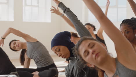 Mujer-De-Yoga-Saludable-Practicando-Pose-De-Curva-Lateral-Sentada-Joven-Musulmana-Con-Pañuelo-En-La-Cabeza-Disfrutando-De-Un-Estilo-De-Vida-Físico-Haciendo-Ejercicio-En-El-Estudio-Con-Un-Grupo-De-Mujeres-Multirraciales