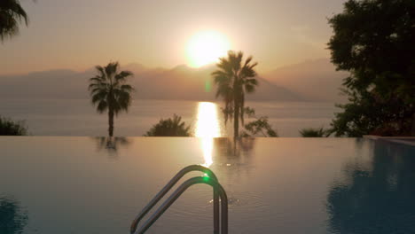 a steadicam shot of an open swimming pool and a sunset by the sea