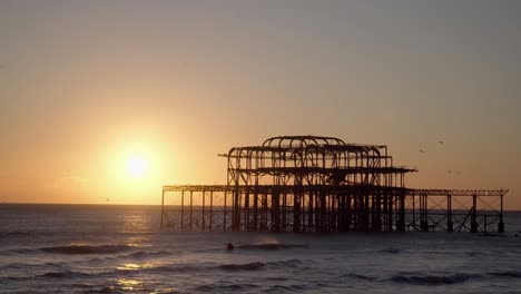 west pier, brighton, silhouetted at sunset with birds flying around