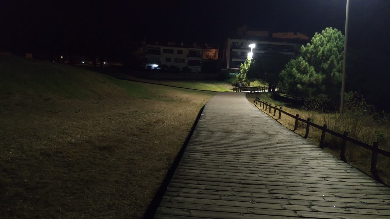 couple of people walking along the overpass built in wood between the lights of the lampposts at night. Blocked panoramic shot Portonovo, Pontevedra, Spain