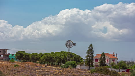 timelapse of white fluffy clouds blowing over windmill and tree line above city