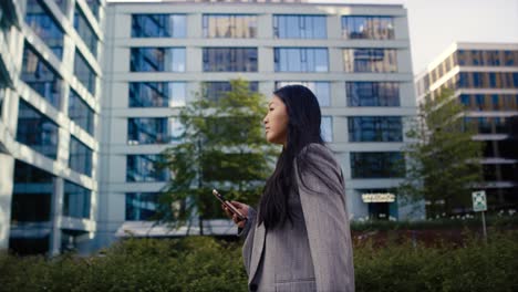 wide shot of cheerful business chinese woman walking in the city and browsing phone