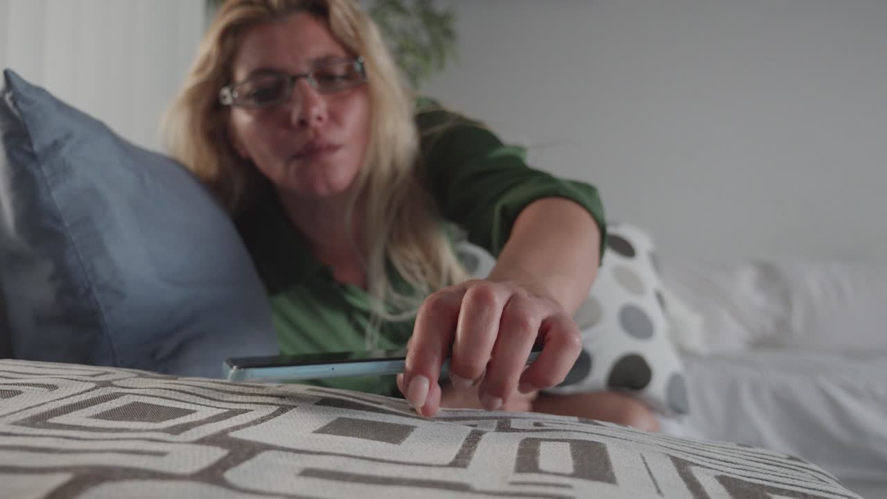 Woman taking smartphone from sofa, addiction to technology
