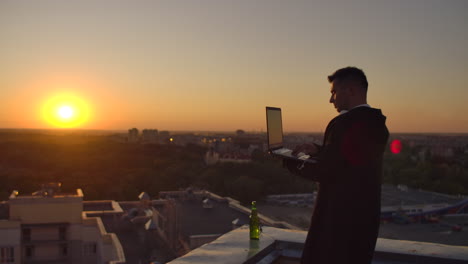 hipster man with a laptop on the edge of the roof. freelancer at work. wireless mobile internet. he works on the internet with headphones and listening music