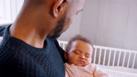 new father cuddling sleeping baby girl in nursery at home