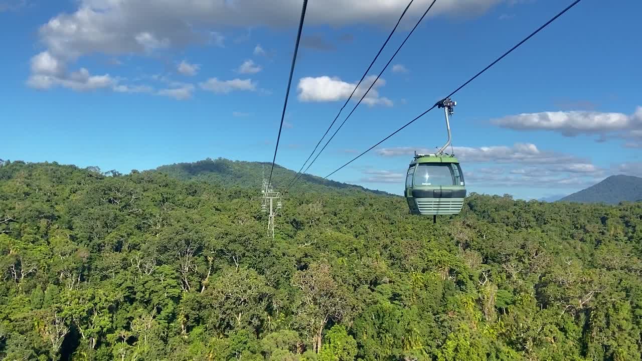 front-facing view from a cablecar, looking along the cables at the approaching cable cars, above the dense green canopy of the rain forest jungle, in tropical North Queensland