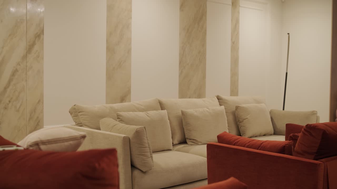 Warm-toned living room with a plush beige sofa, accented by vibrant red pillows, against a backdrop of elegant marble columns for a luxurious touch