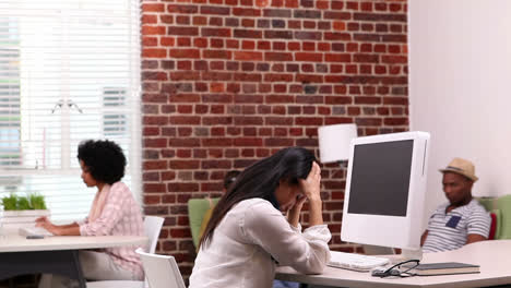 una mujer de negocios casual tiene dolor de cabeza en su escritorio.