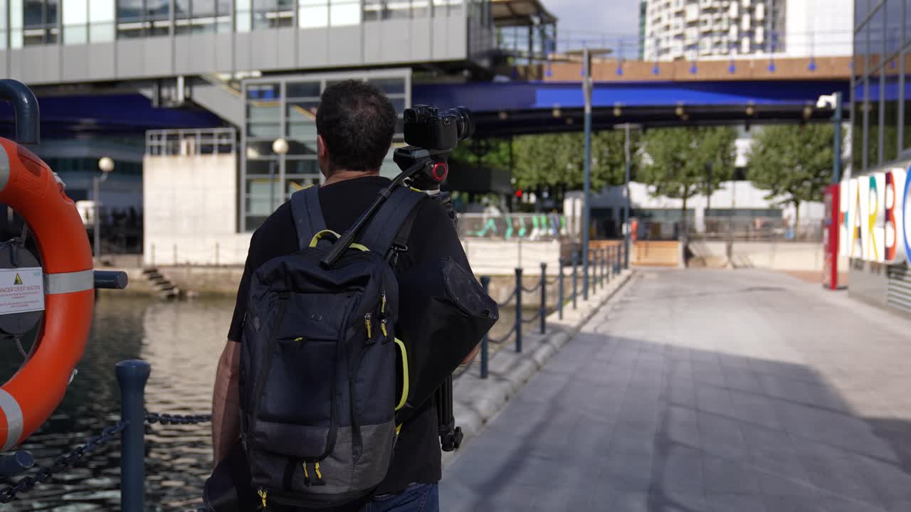 도시에서 비디오를 촬영하기 위해 카메라와 삼각대를 들고 가는 청년