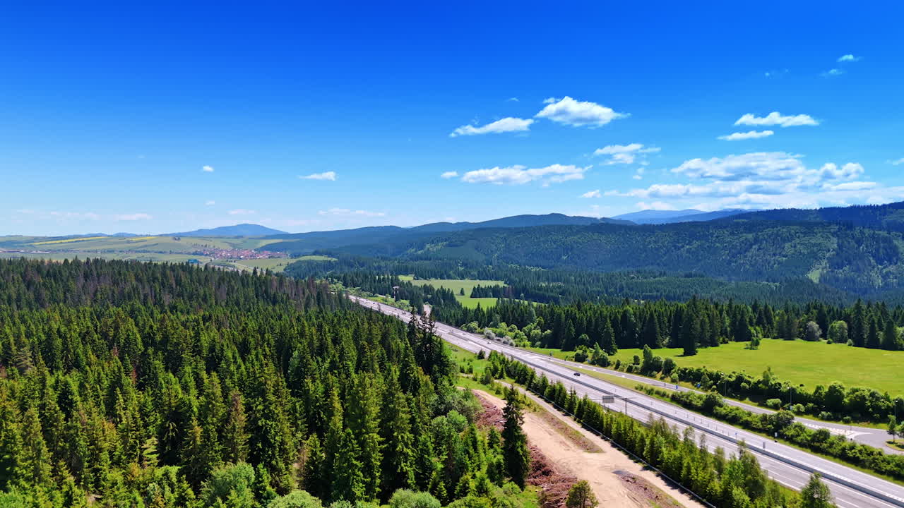 Modern highway crossing a beautiful nature landscape. A village can be seen at backdrop. Tatra mountain range in Slovakia at backdrop. Aerial view