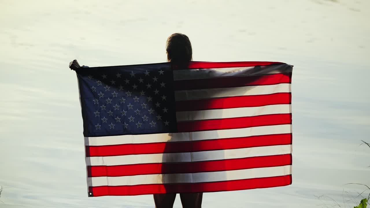 Slow motion silhouette of woman raising US flag against morning river light