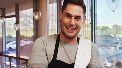 Smiling-waiter-leaning-on-glass-door-in-cafÃ©