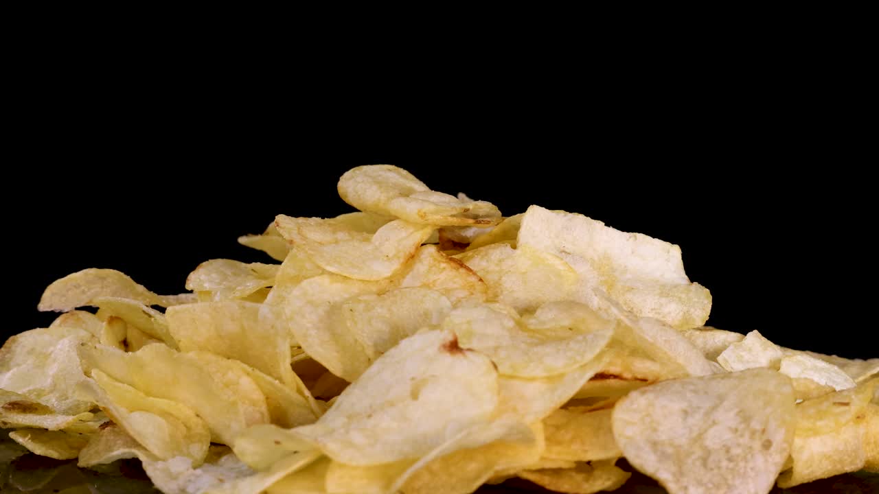 Golden potato chips cascade onto a heap, captured in slow motion with dramatic studio lighting