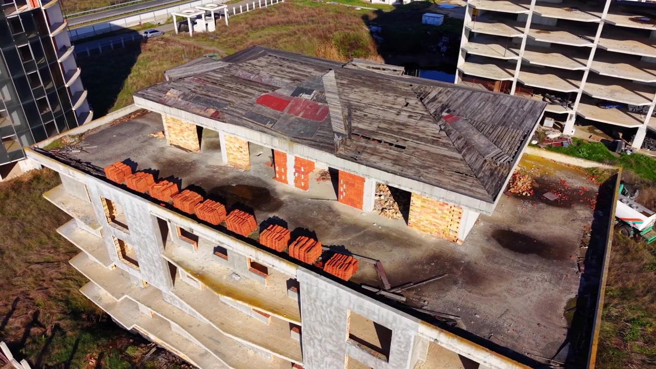 Daytime aerial of rooftop under construction with stacked tiles. Overhead view shows wooden shingles, brick pillars and orange roof tiles stacked below.