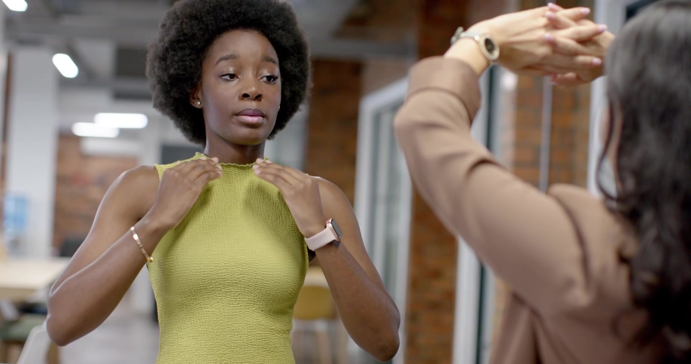 Mulheres diversas fazendo alongamentos de pescoço e braços para uma pausa rápida no escritório, com a de blusa verde-limão liderando, observando.