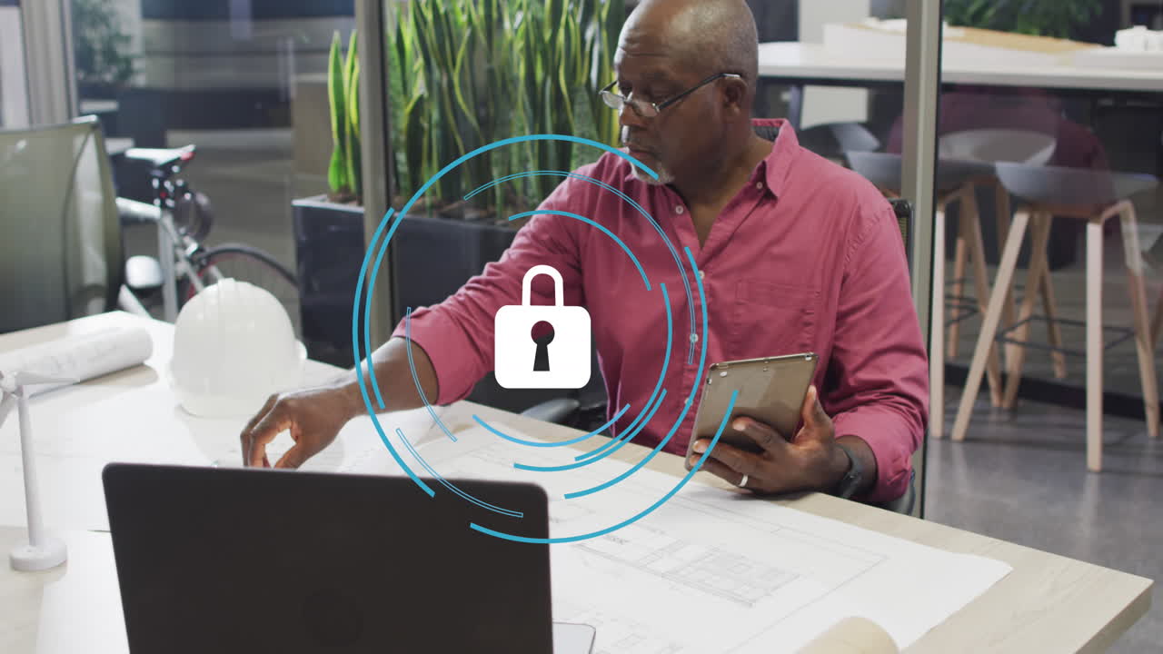 Animation of security padlock icon over african american man working on his plan at office