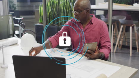 animation of security padlock icon over african american man working on his plan at office