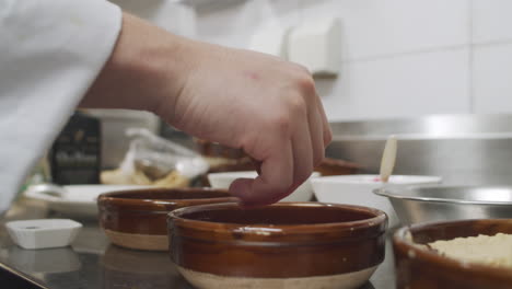 chef plating the dish in restaurant kitchen, adding spices into small ceramic bowl