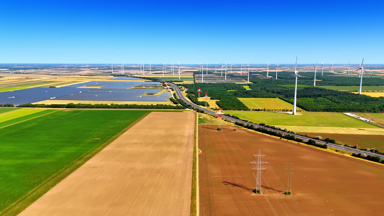 Wind turbine energy landscape. Aerial view of a vibrant agricultural landscape featuring wind turbines and solar panels under a clear blue sky