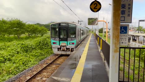 pan from left to right following a local train departing a rural station in japan