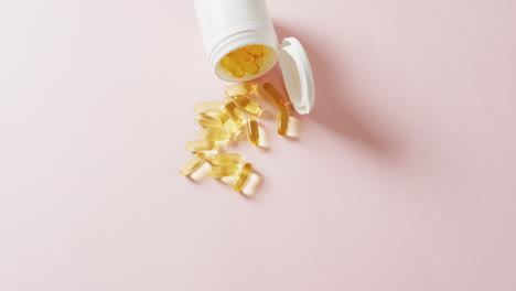 video de una caja de pastillas blanca derramando cápsulas de aceite sobre un fondo rosa con espacio para copiar