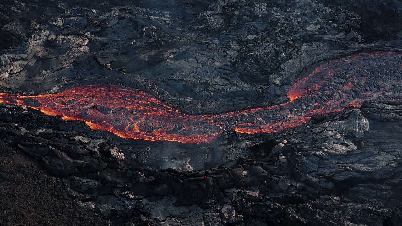 Un fiume di lava scorre sulla superficie terrestre circondato da roccia basaltica scura.