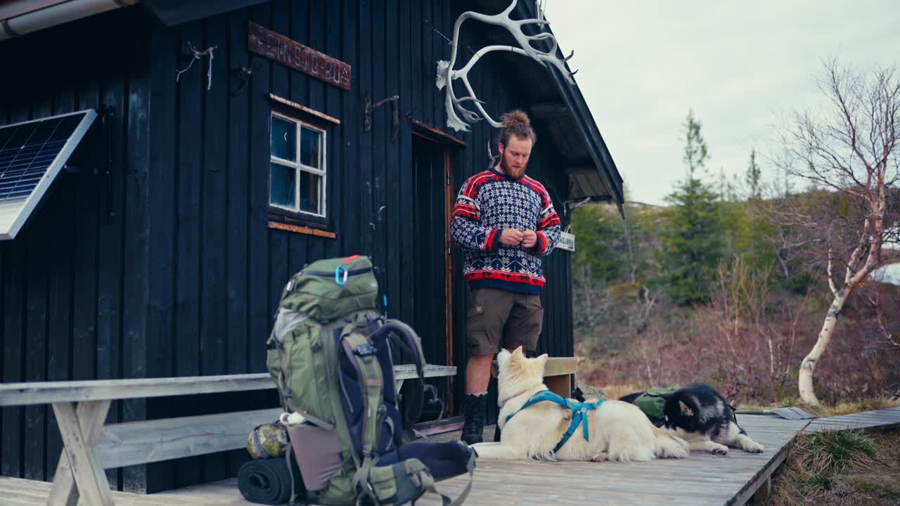 A Hiker Stands With His Two Dogs in Front of a Rustic Cabin Near Reinsjøen in Åfjord, Trøndelag, Norway - Static Shot