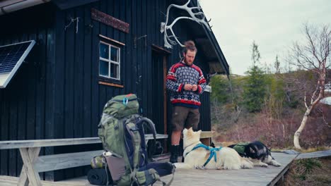 a hiker stands with his two dogs in front of a rustic cabin near reinsjøen in åfjord, trøndelag, norway - static shot