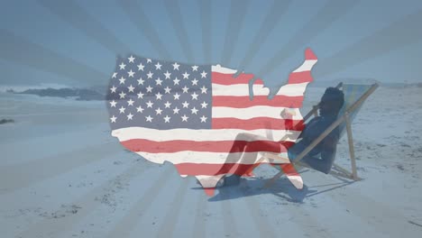 Animation-Einer-Karte-Mit-Amerikanischer-Flagge,-Die-über-Einem-Mann-Weht,-Der-Im-Liegestuhl-Am-Strand-Etwas-Trinkt