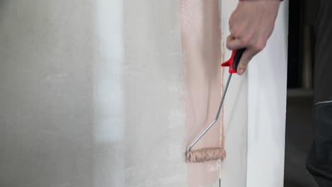 close up of man´s hand painting a wall in pink color with paint roller