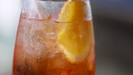 primer plano de un spritz de aperol refrigerado con rebanada de limón, destacando la condensación y los colores vibrantes en una iluminación suave