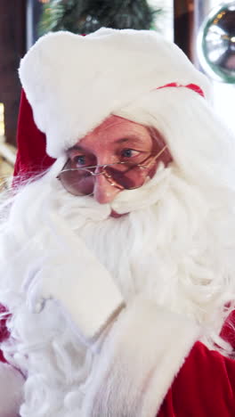 portrait of santa claus is sitting at the table on christmas. santa querrels to someone showing hand gesture indoors. vertical video