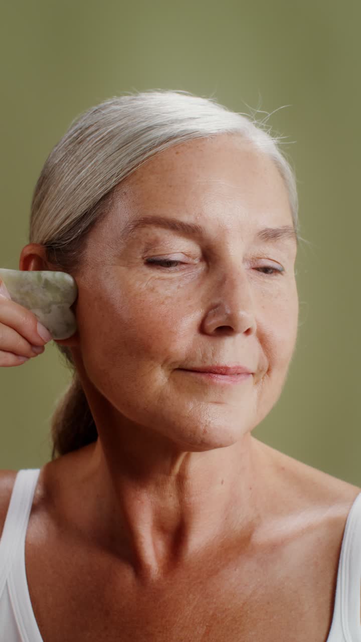 Senior woman using gua sha tool for face massage