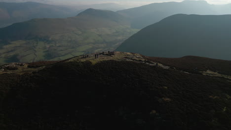 Flying-towards-hikers-on-mountain-summit-with-misty-mountains-in-distance-in-English-Lake-District-UK