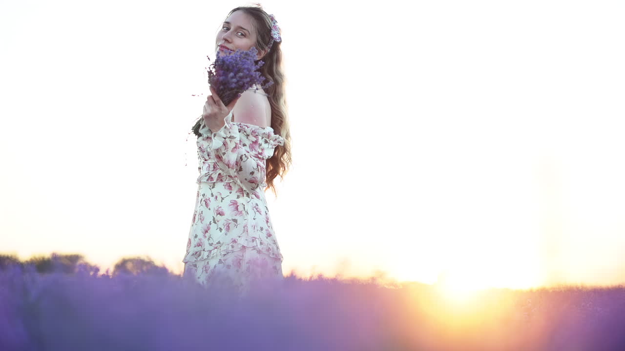 Close up of lavender flowers in full bloom with a blurred woman in a floral dress walking in the background