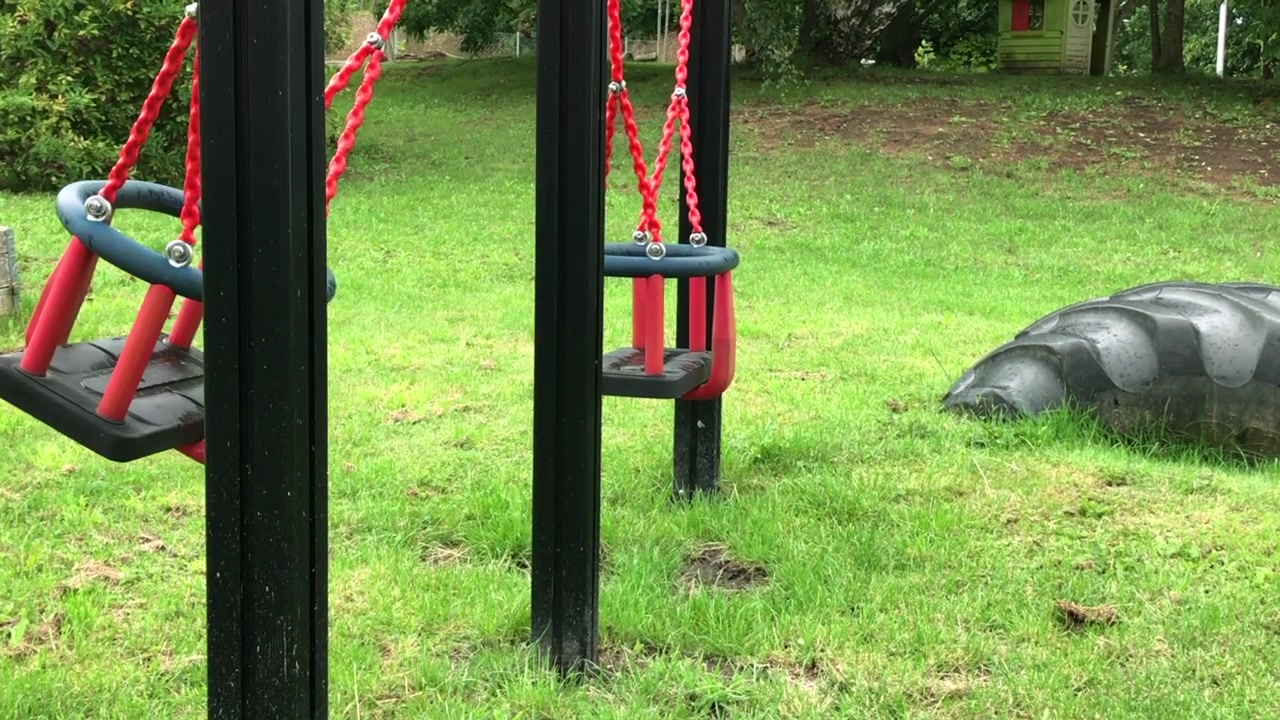 Close up video of a lone red swing fluctuating back and forth in an empty playground in Eslöv, Sweden