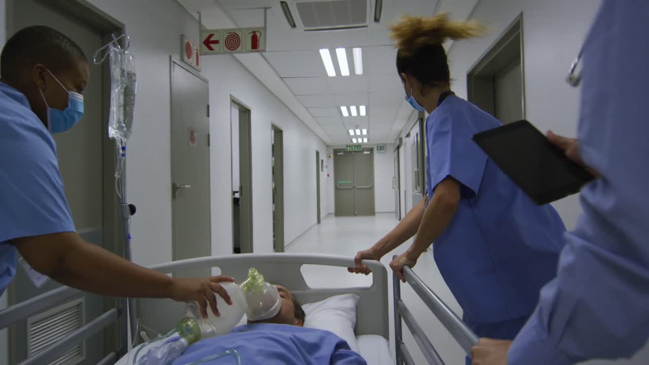 Grupo de médicas de etnias diversas usando máscaras faciais e empurrando um paciente em uma cama no corredor do hospital