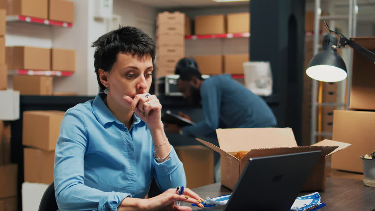 Woman working at desk in warehouse with boxes and employees