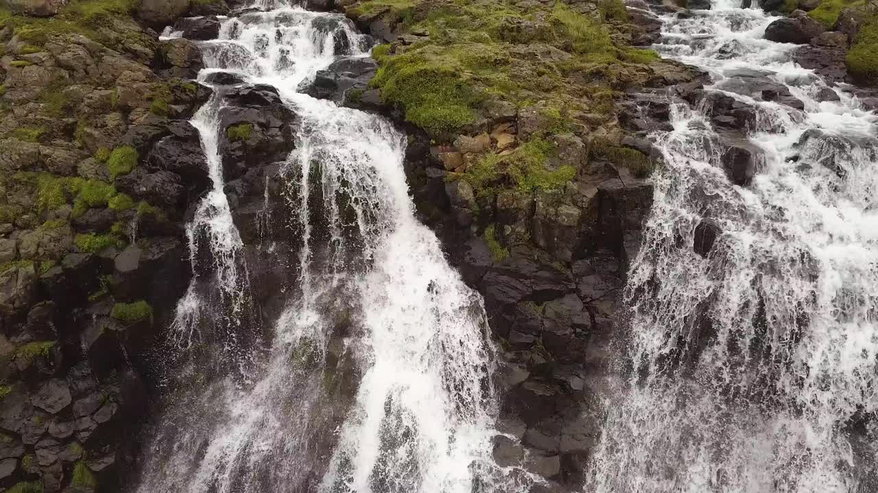 primer plano aéreo inclinado de las cascadas de glymur que fluyen por un acantilado rocoso empinado, en verdes tierras altas durante el día, islandia