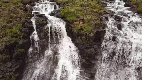 aerial close up tilting of glymur waterfalls streaming down steep rocky cliff, in verdant highlands at daytime, iceland