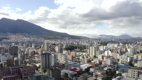 drone shot of the north part of the city of quito, ecuador. overlooking buildings and in the back, pichincha mountain and its antennas. also, trees and houses of the city.