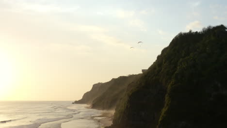 Dos-Parapentes-Volando-Sobre-Acantilados-épicos-Que-Bordean-La-Playa-De-Melasti,-Al-Sur-De-Bali,-Vía-Aérea