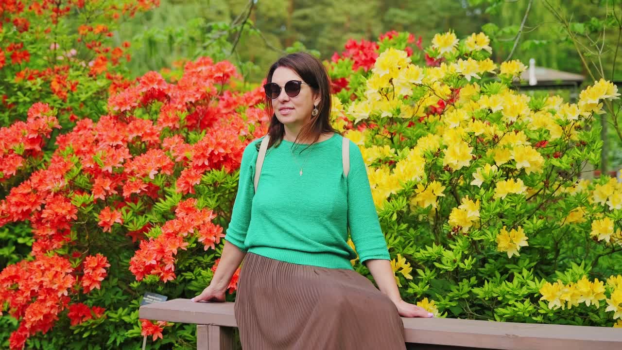 Donna di mezza età seduta su una panchina da giardino tra rododendri in fiore, Babite, Lettonia.