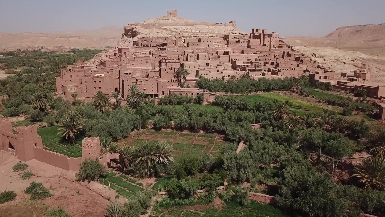 ワルザザートにあるユネスコ世界遺産、アイト・ベン・ハドゥのカスバの空撮。豊かなオアシスとヤシの木立を見下ろしています。旅行や映画のような映像に最適な象徴的なモロッコのランドマークです。
